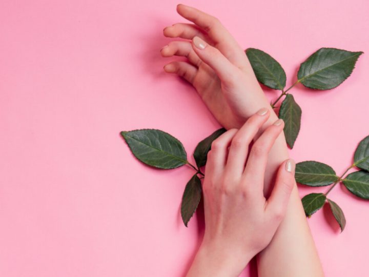 Women's hands against a pink background applying organic skincare