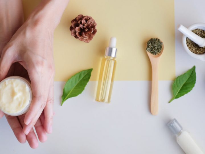 Women's hands against a yellow and white background applying organic skincare cream.